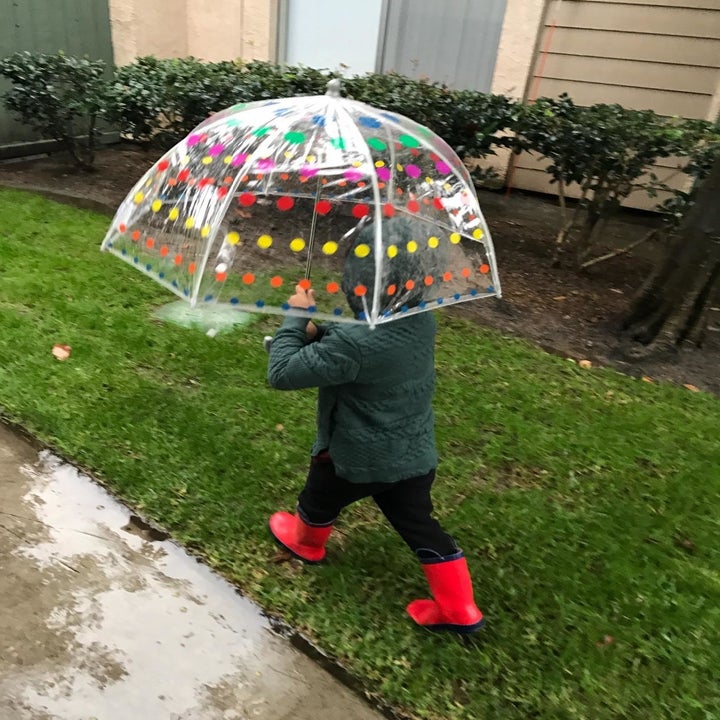 Reviewer's child walking in the rain holding the clear umbrella with colorful dots