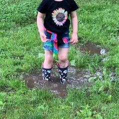 Reviewer's child wearing the boots and knee-deep in a muddy puddle