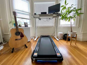 reviewer photo of the folded treadmill under a desk, next to a guitar