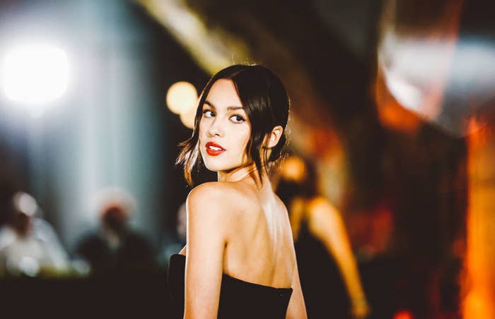 Olivia looking over her shoulder as she poses on a red carpet in a strapless dress