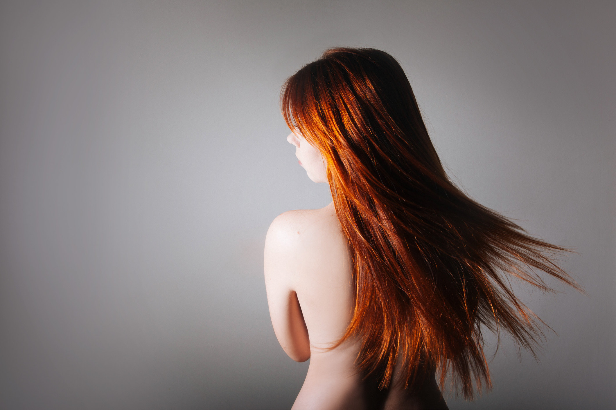 The bare back of a redheaded woman, showing her face in profile