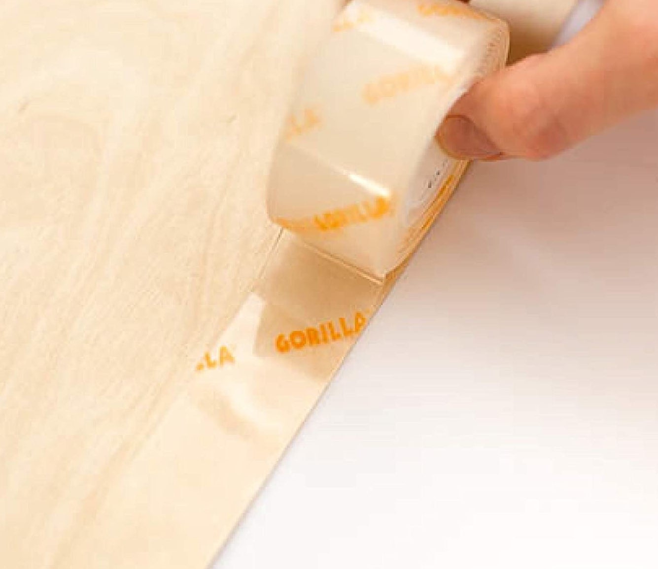 a person rolling the extra-strong mounting tape across the edge of a wooden surface