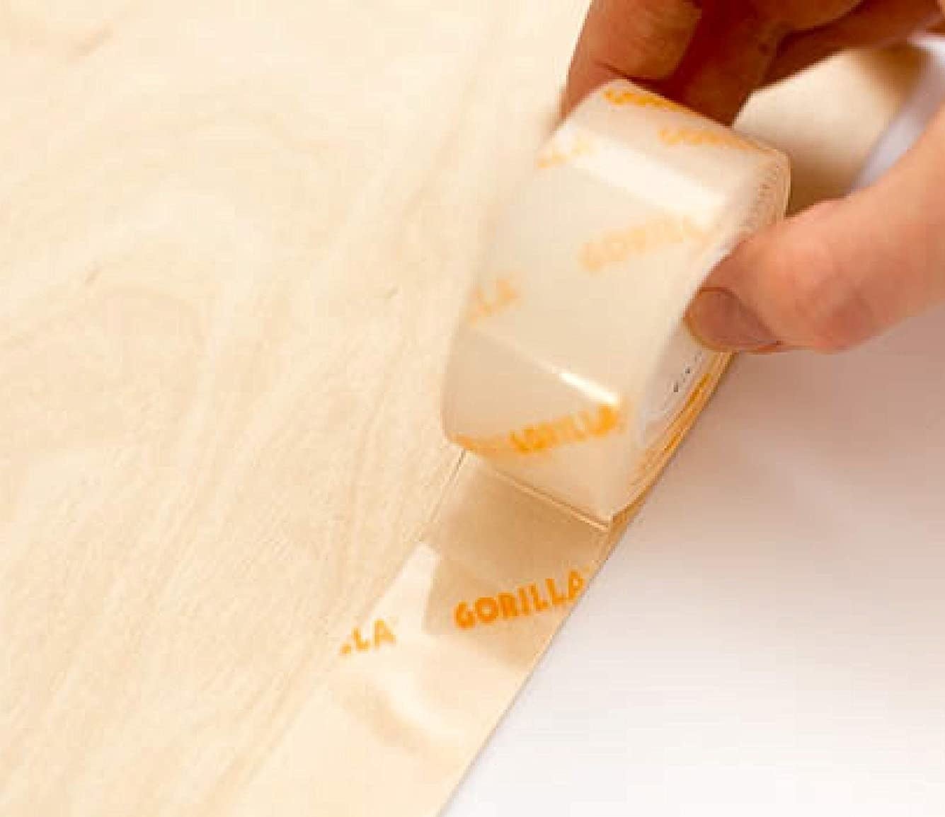 a person rolling the extra-strong mounting tape across the edge of a wooden surface