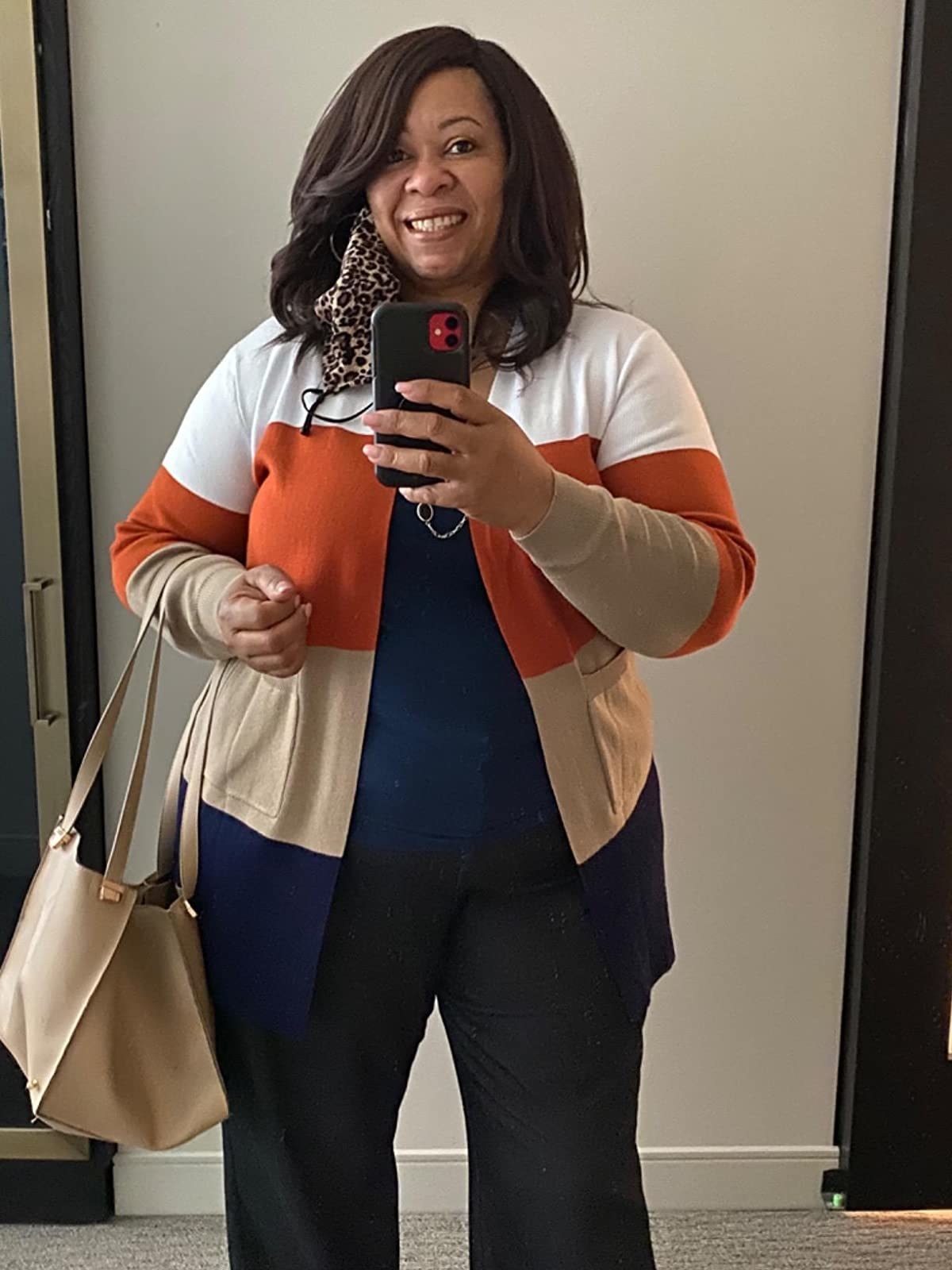 Reviewer is wearing an orange, tan, blue, and white color block cardigan with a blue top and black pants