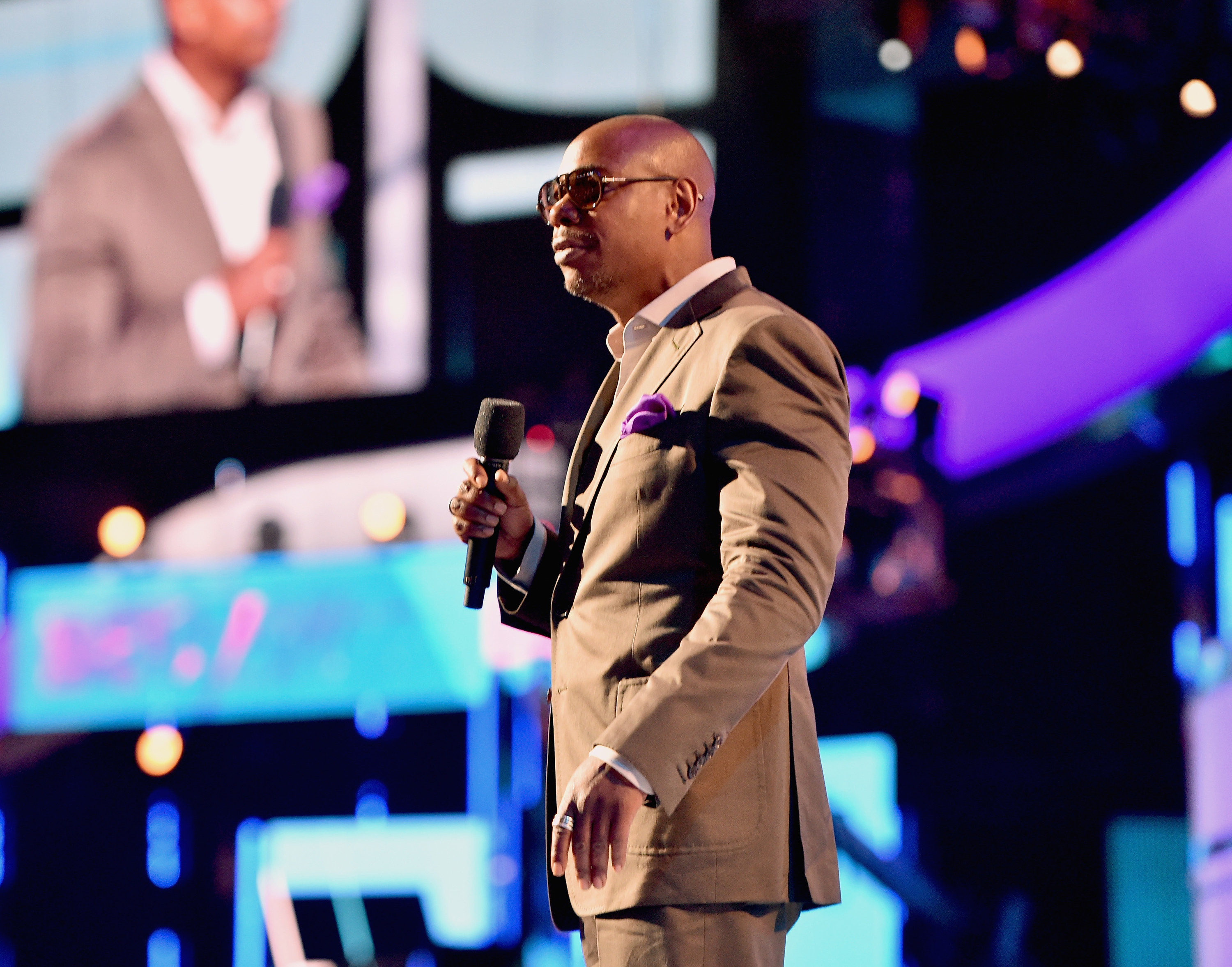 Chappelle standing onstage and looking dapper in a suit