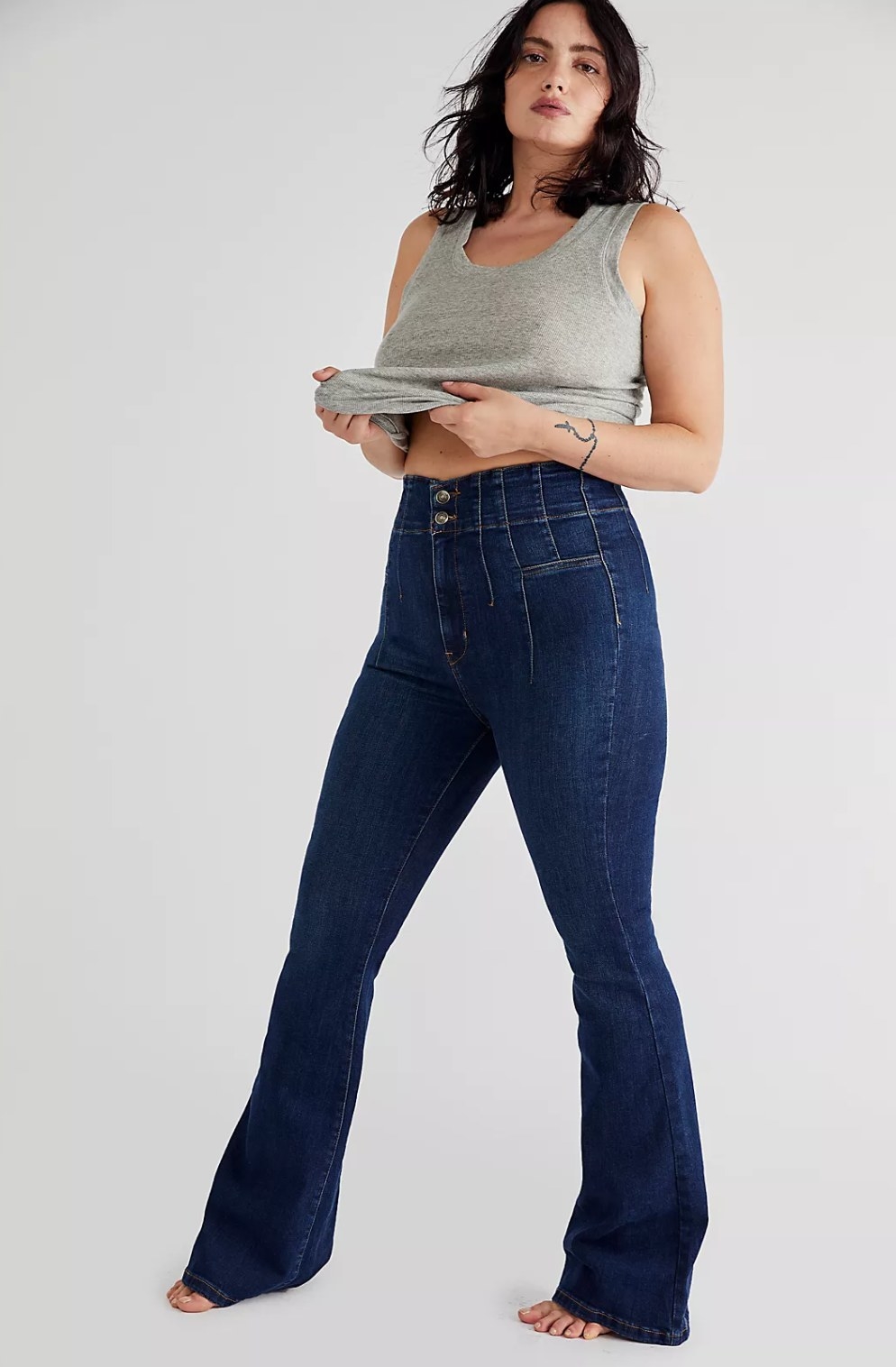 model wearing the dark blue flare jeans and a gray tank top holding it up and out in front of them