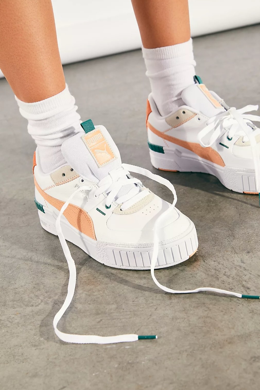 model's legs wearing the puma sneakers in white with light orange and green accents and ankle high white socks