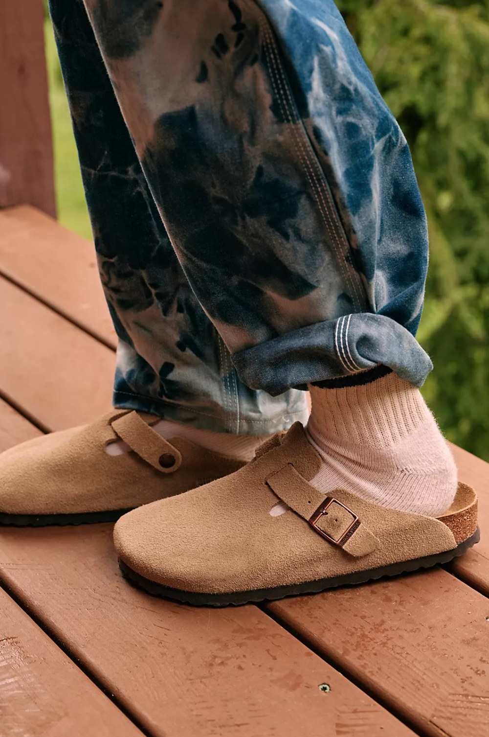 model wearing the tan birkenstocks with white socks and blue patterned pants on a wooden deck