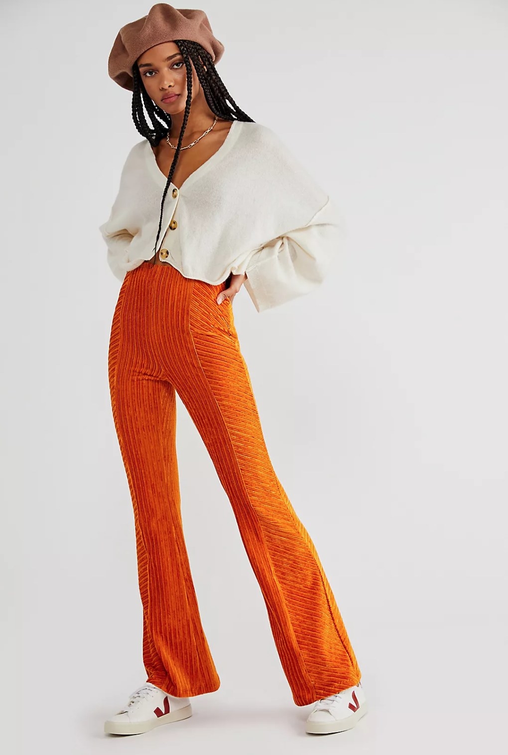 model wearing the velvet pants in bright orange with a cream cardigan, white sneakers, and a brown hat