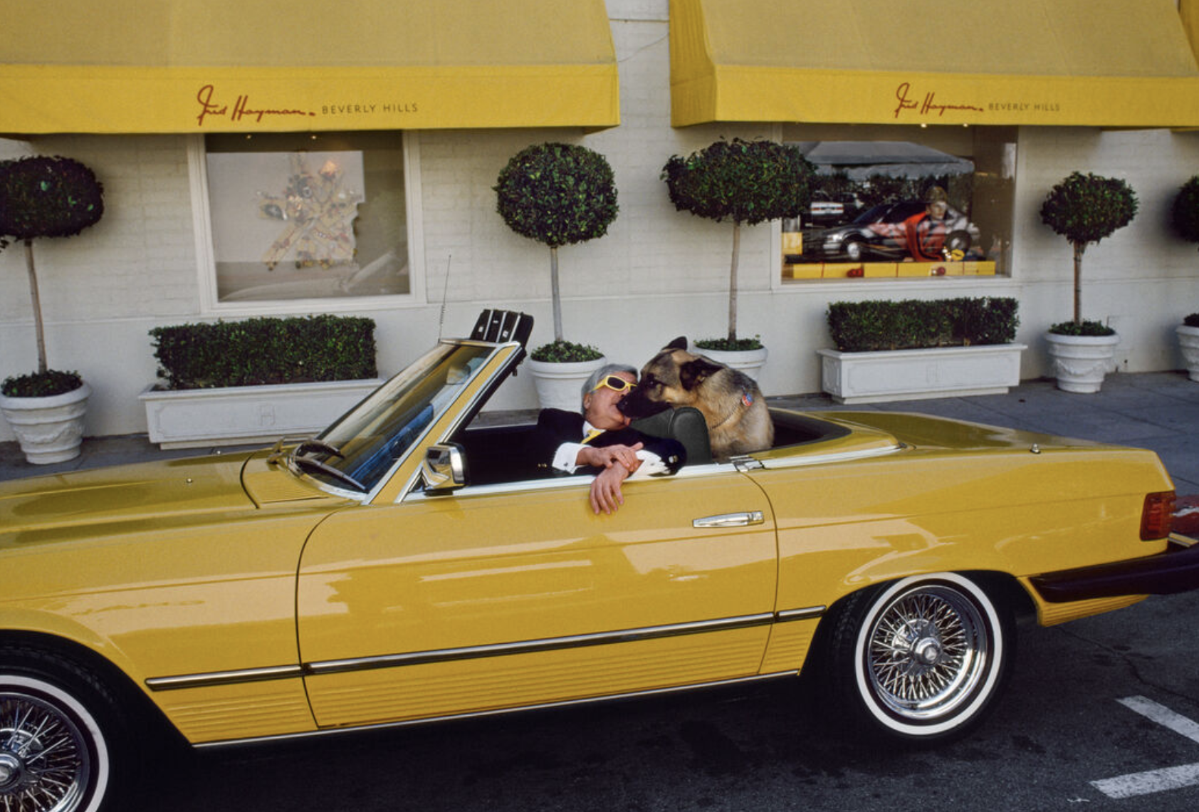 Man seen kissing a dog as they both sit in a bright yellow convertible