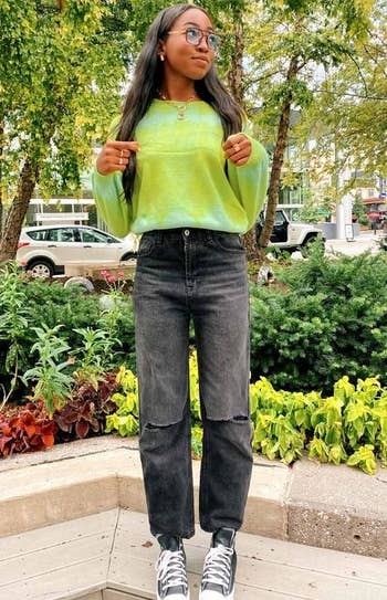 model wearing the jeans with black Converse and a green sweater