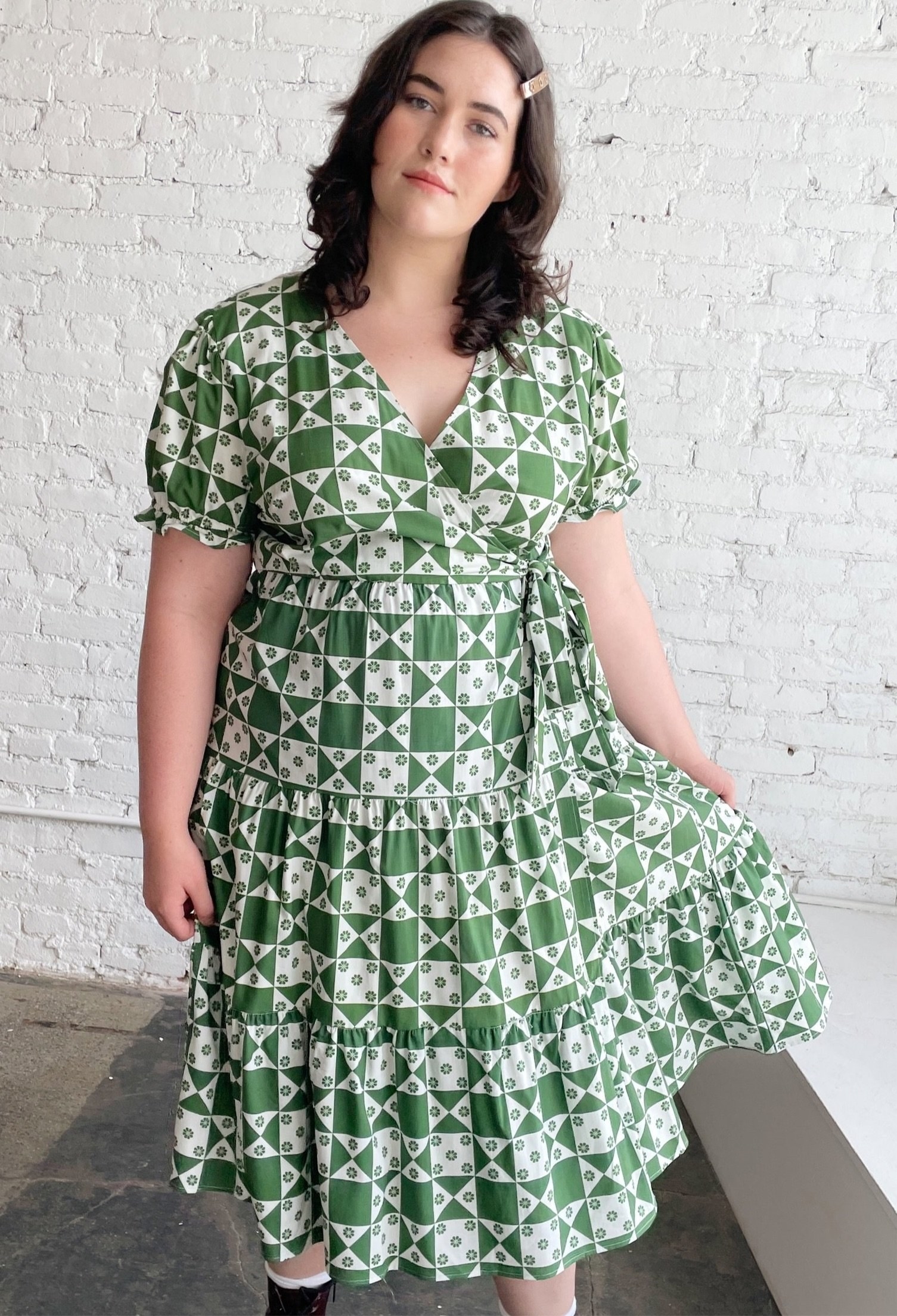 model wearing the puff-sleeve wrap dress with green and white quilt-like pattern and small green flowers all over it