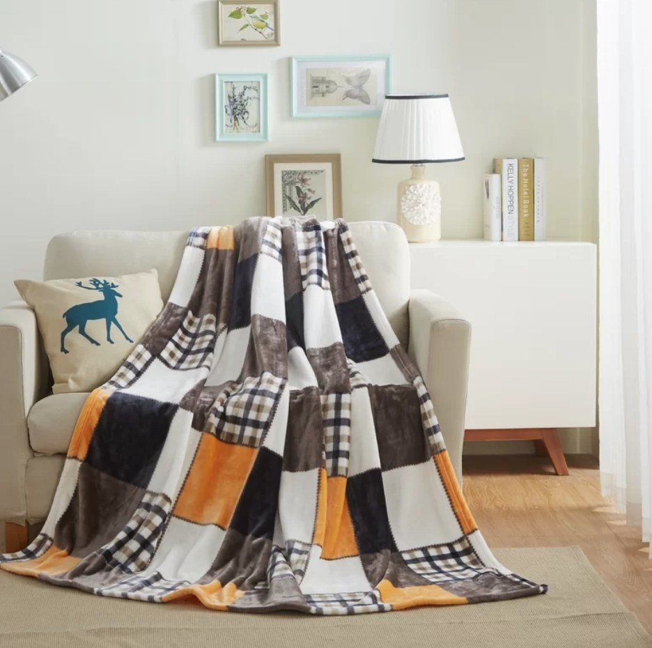 An orange/brown plaid &amp;amp; patchwork fleece throw draped over a chair