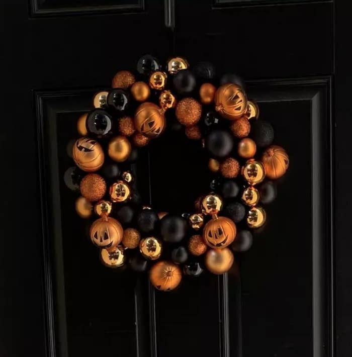 jack-o&#x27;-lantern wreath with orange, black and gold ornaments on black door