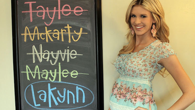 A woman stands in front of a chalkboard with 4 names crossed out and the name Lakynn circled