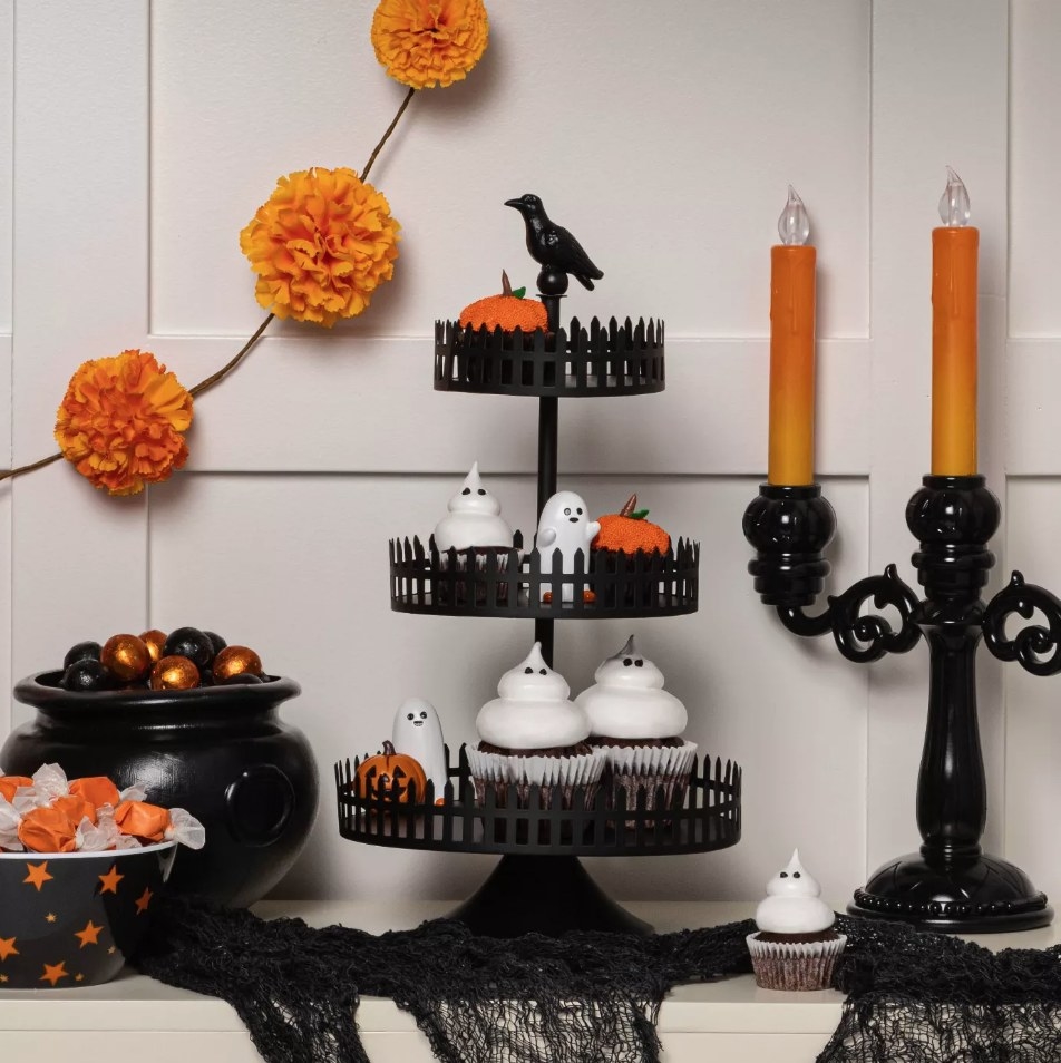 Black three tiered tray holding cupcakes on bottom tier, ghost and pumpkin figurines on middle tier, pumpkin decoration on top