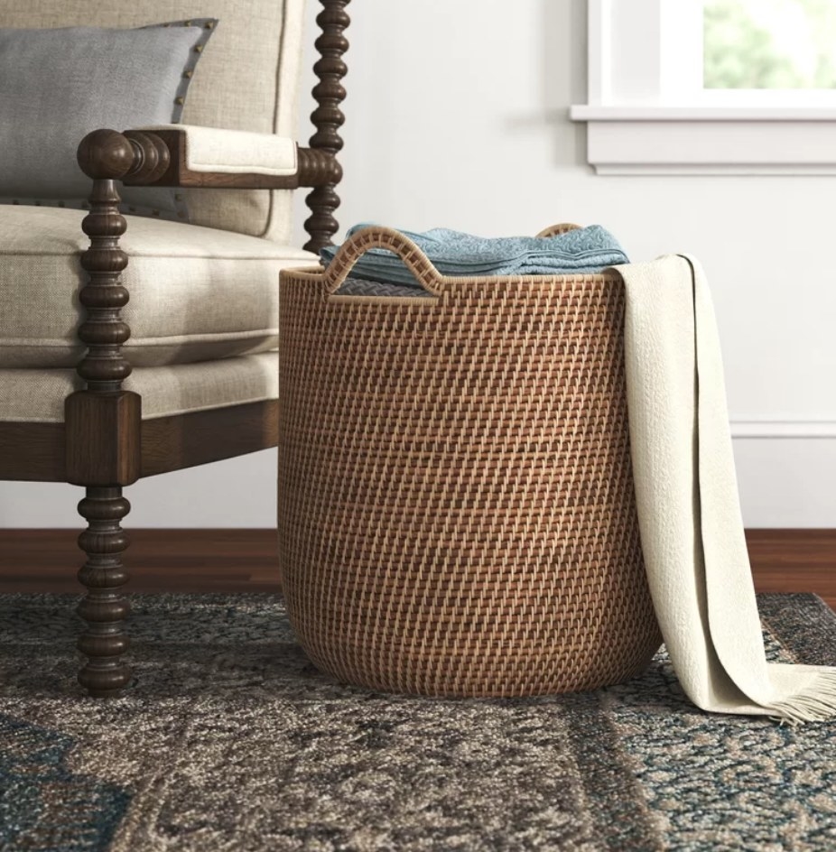 A round, brown rattan basket filled with blankets next to an accent chair