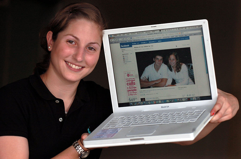a girl holding up her facebook profile on a laptop