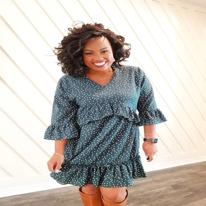 A reviewer wearing the three quarter-sleeve dress in teal with white polka dots with boots