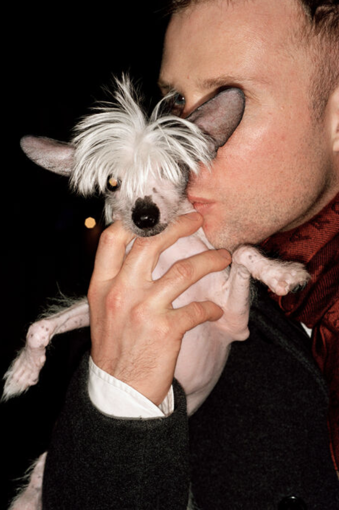 A man holds a small dog in his hand and gives it a kiss