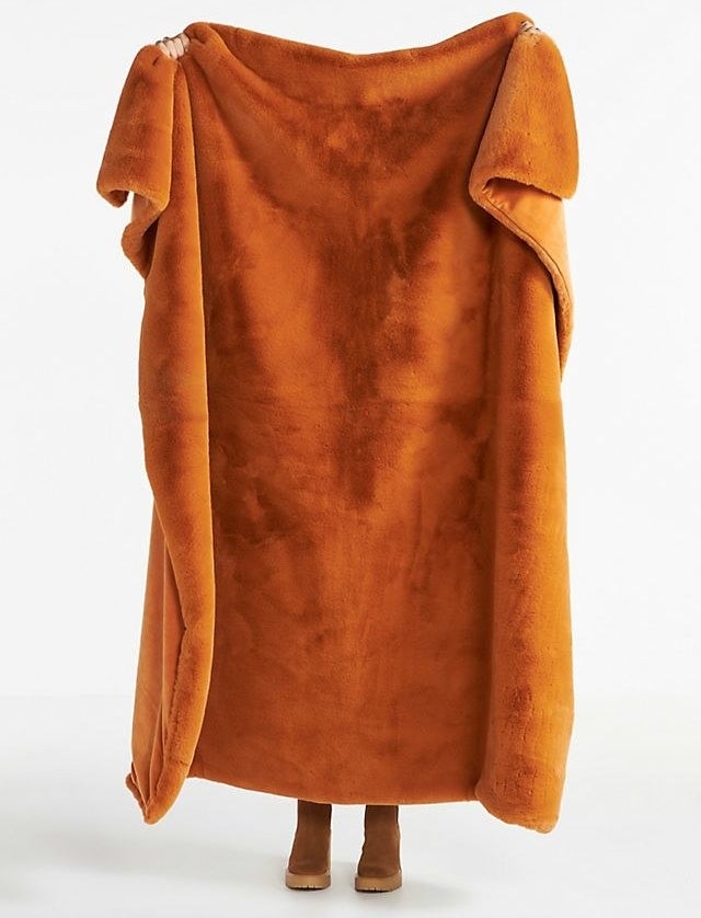 An orange blanket being held up in front of someone, covering their entire body