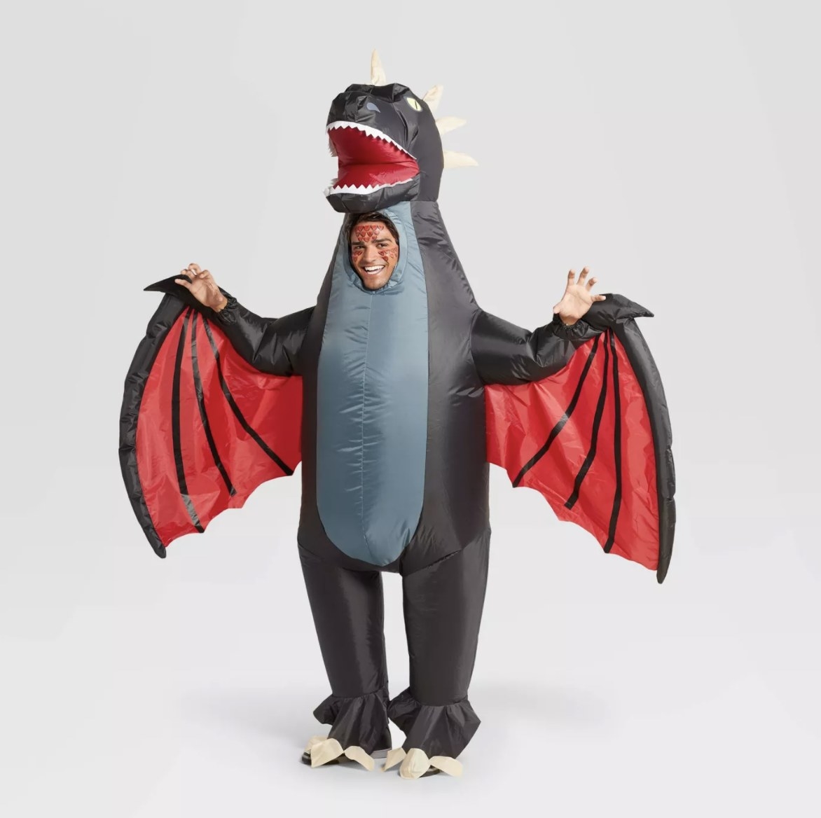 An adult wears a grey, black and red dragon costume that has wings, a head and legs complete with spikes and talons
