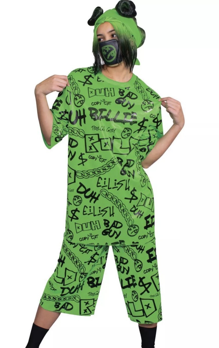 An adult is in a bright green outfit with &quot;DUH,&quot; &quot;BILLIE&quot; and &quot;EILISH&quot; written all over in script font with a black mask and green and black hair with space buns.
