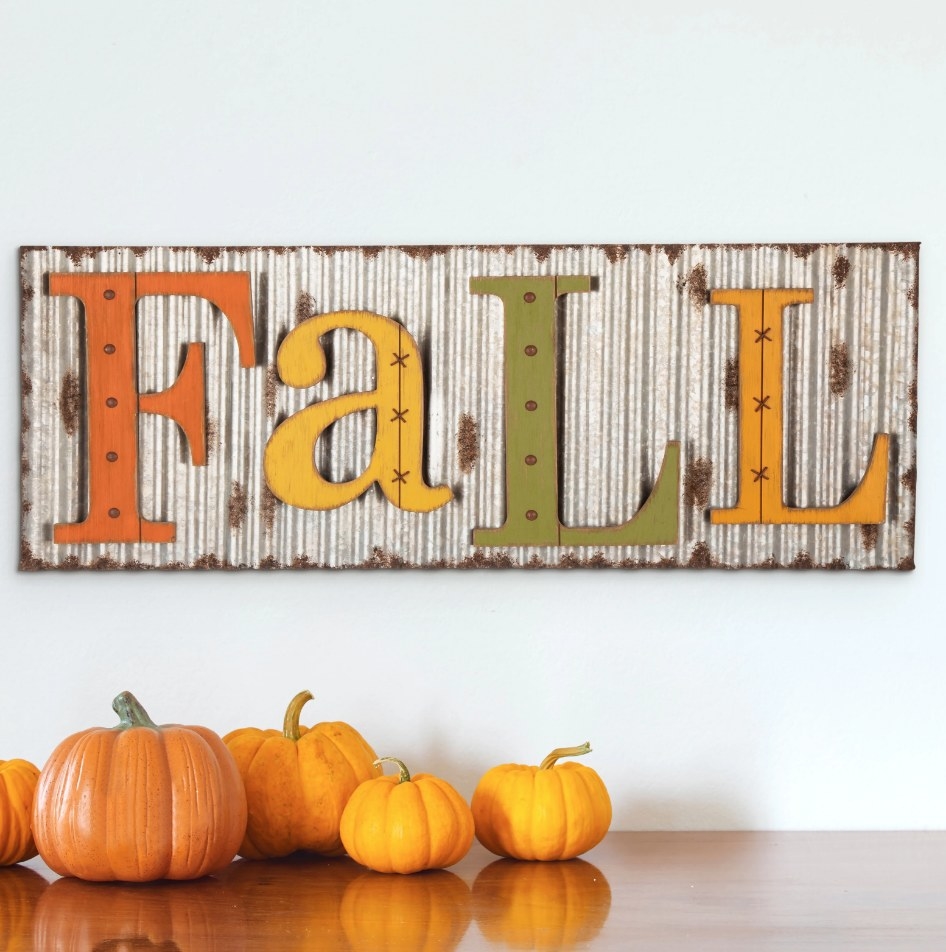 A metal, hanging wall sign that says "Fall" in orange/yellow/green letters