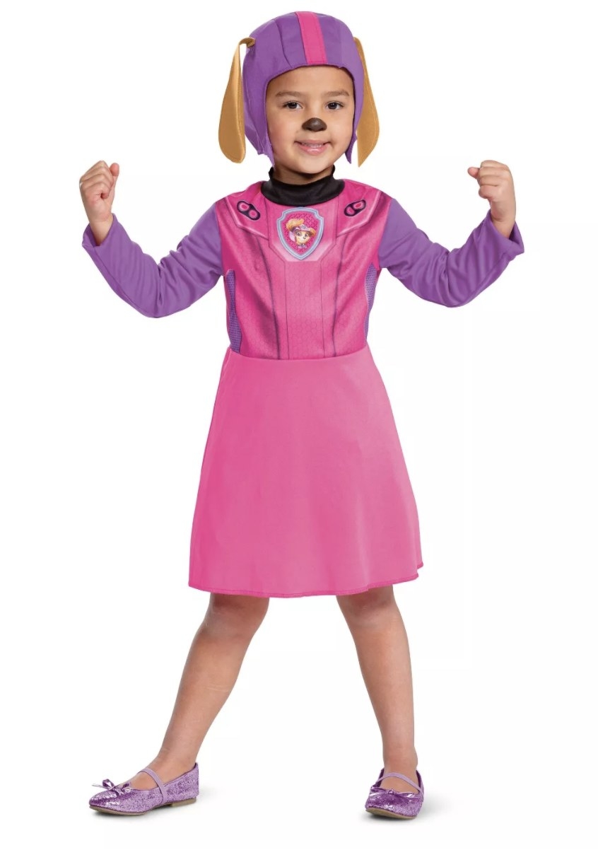 A child wears the purple and pink dress with a badge and a purple and pink headpiece with brown floppy ears