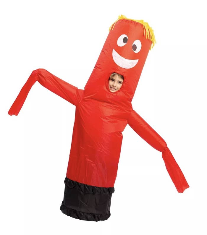A child is in an inflatable red tube costume that has a small black base, a silly face and yellow stringy hair