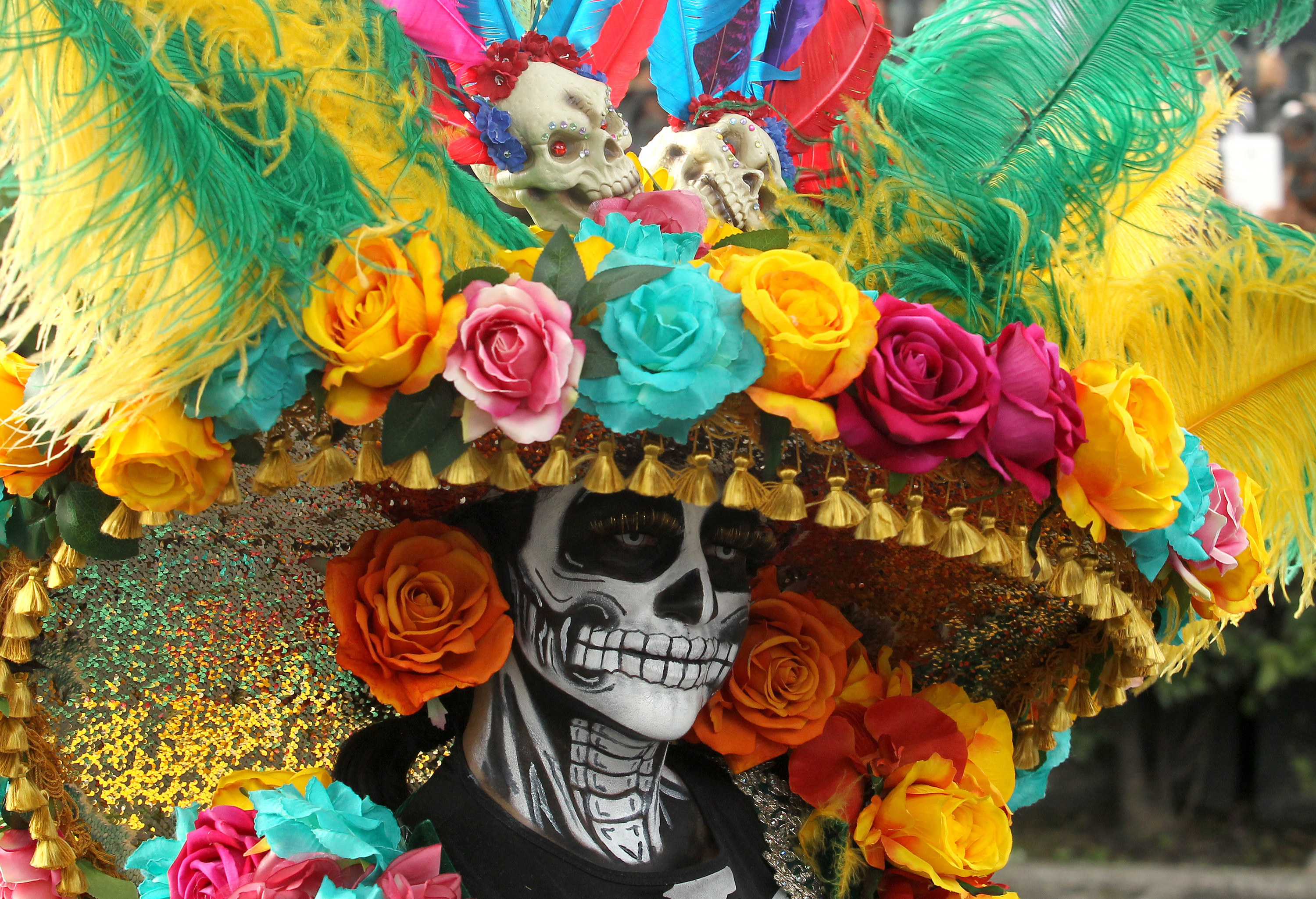 Person with skull  paint surrounded by ornate head gear with colorful flowers