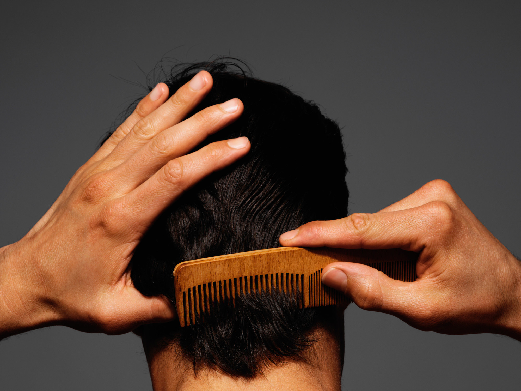 Person with short hair runs a comb through their scalp