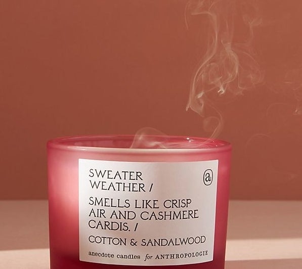 A red candle with a white label that says "Sweater Weather / Smells like crisp air and cashmere cardis / Cotton &amp;amp; sandalwood"