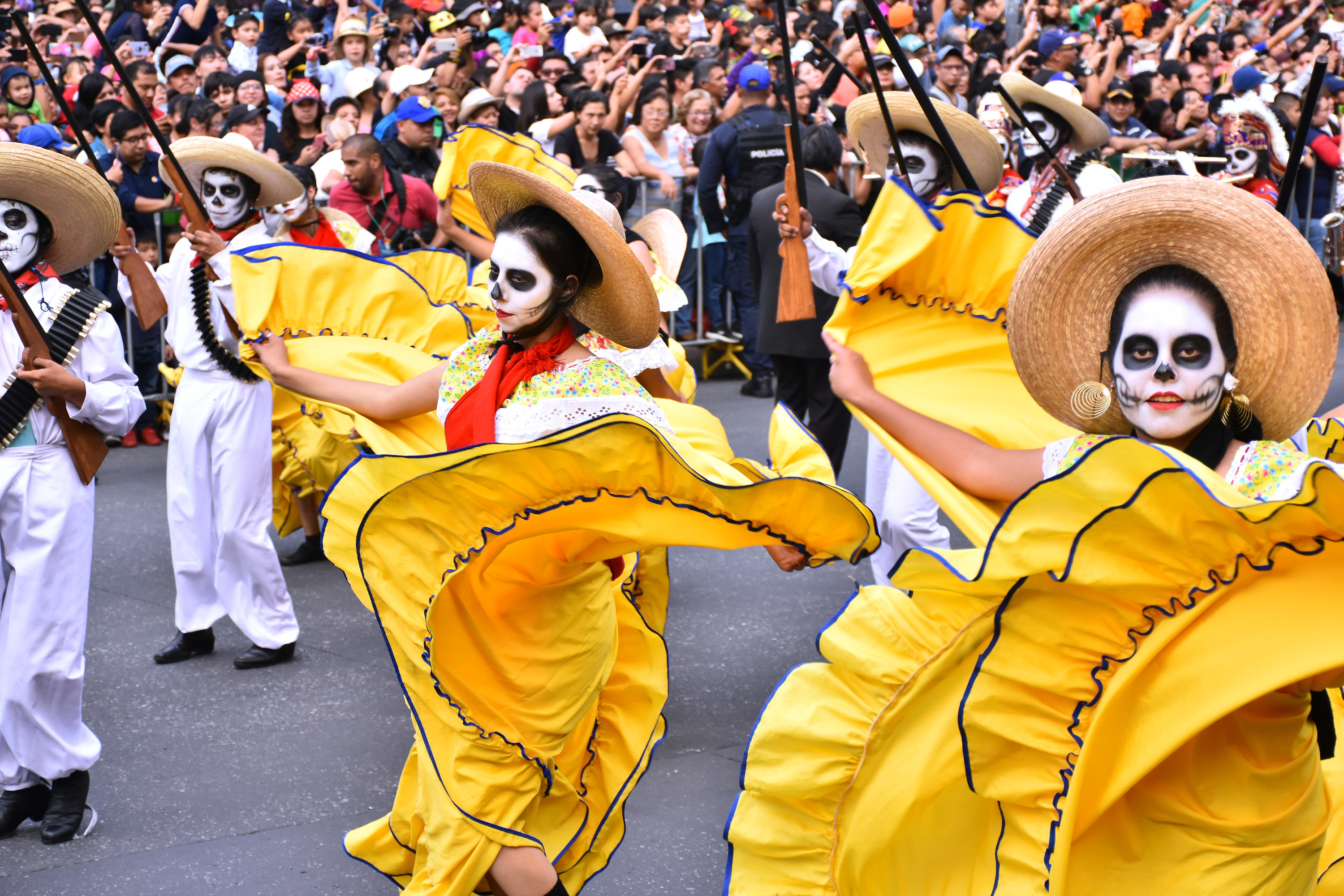 People wearing skull paint and bright yellow costumes holding guns in the air