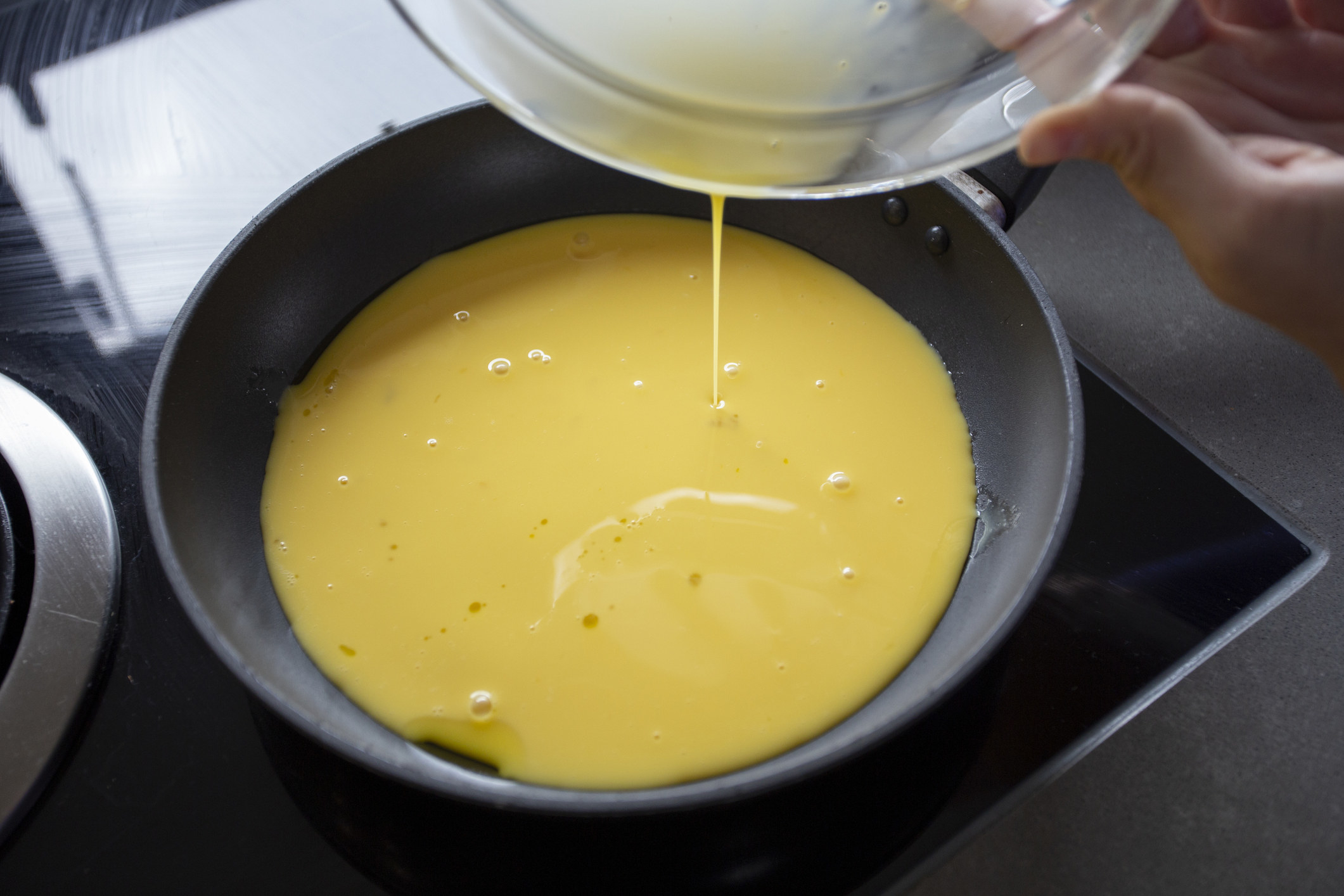 Pouring beaten eggs into a skillet.