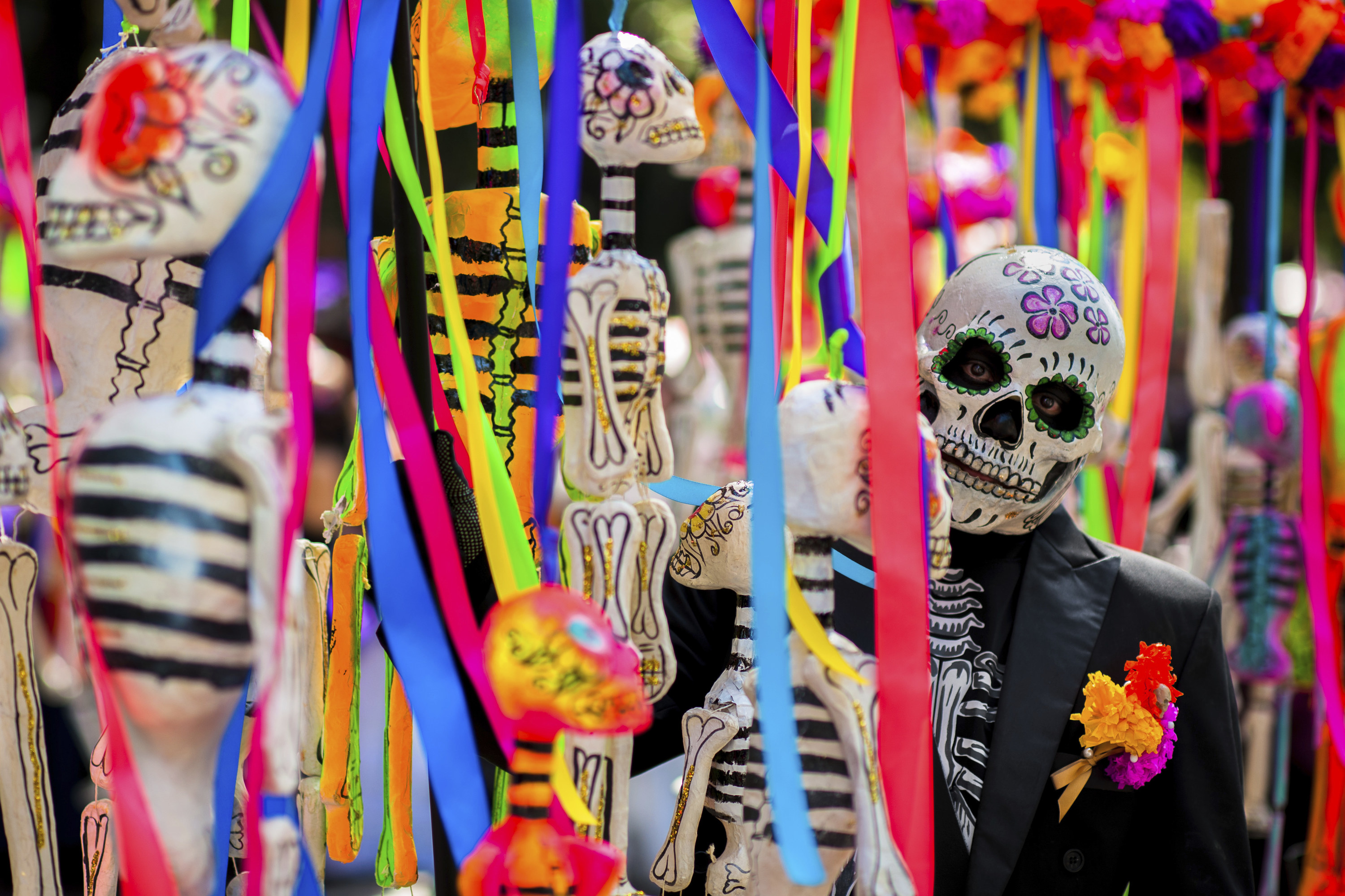 A man with a skull mask stands amid other decorations including skeletons
