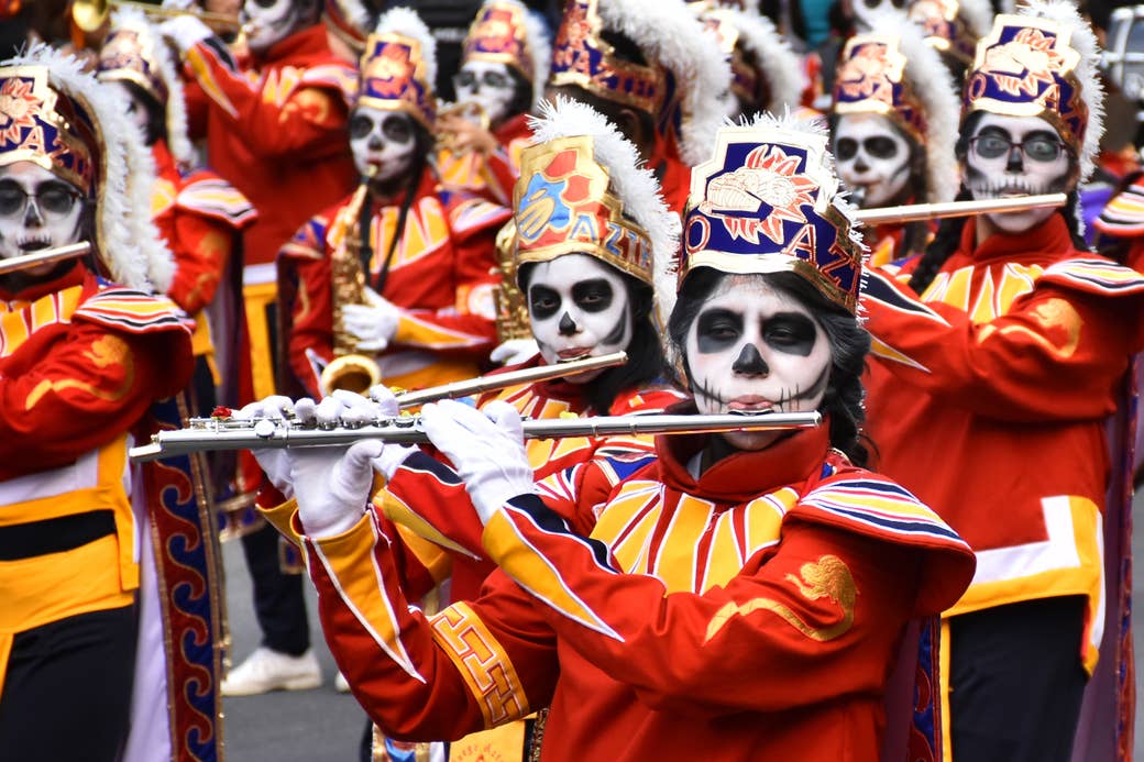 Costumed people wearing skull makeup and head gear play flutes and other instruments