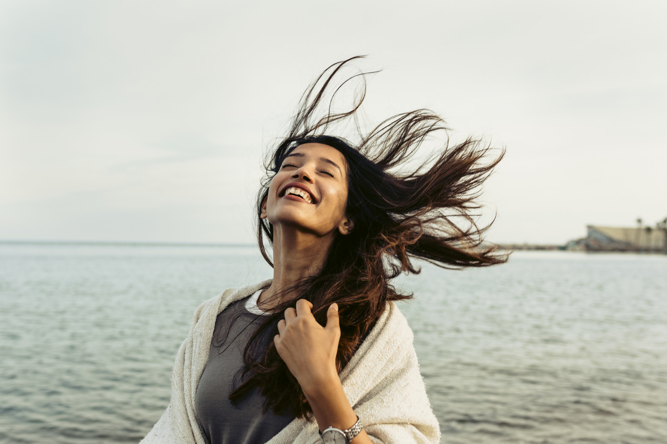 Person stands by a body of water as wind blows through their hair