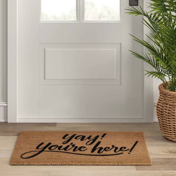 The doormat with a brown background and black writing underneath a door