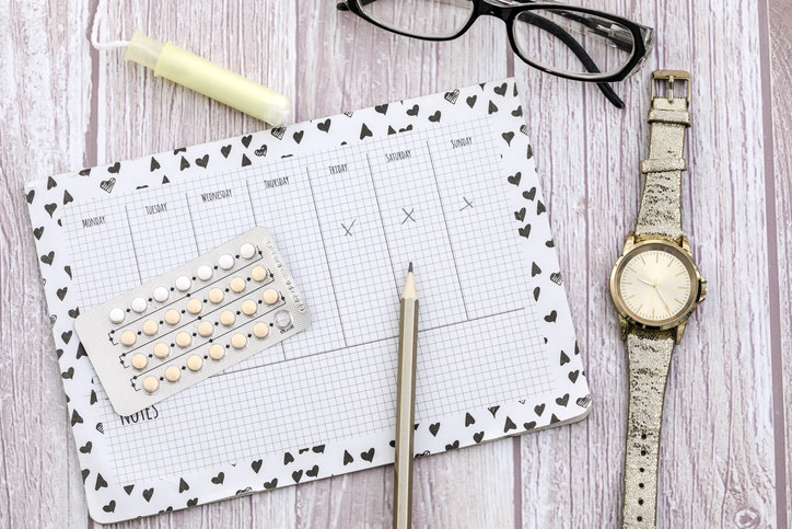 A calendar surrounded by EC pills, a watch, a pair of eyeglasses, and a tampon