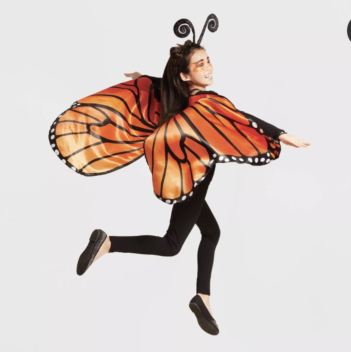 A child wears the orange and black wings and jumps into the air