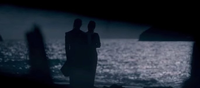 Two figures are silhouetted against the ocean