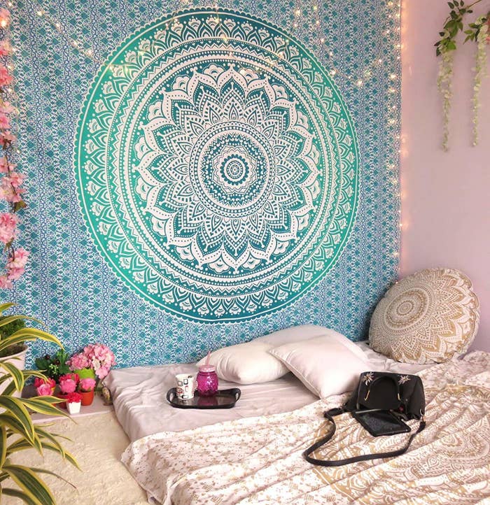 A Mandala tapestry on a wall with a bed on the floor in front of it