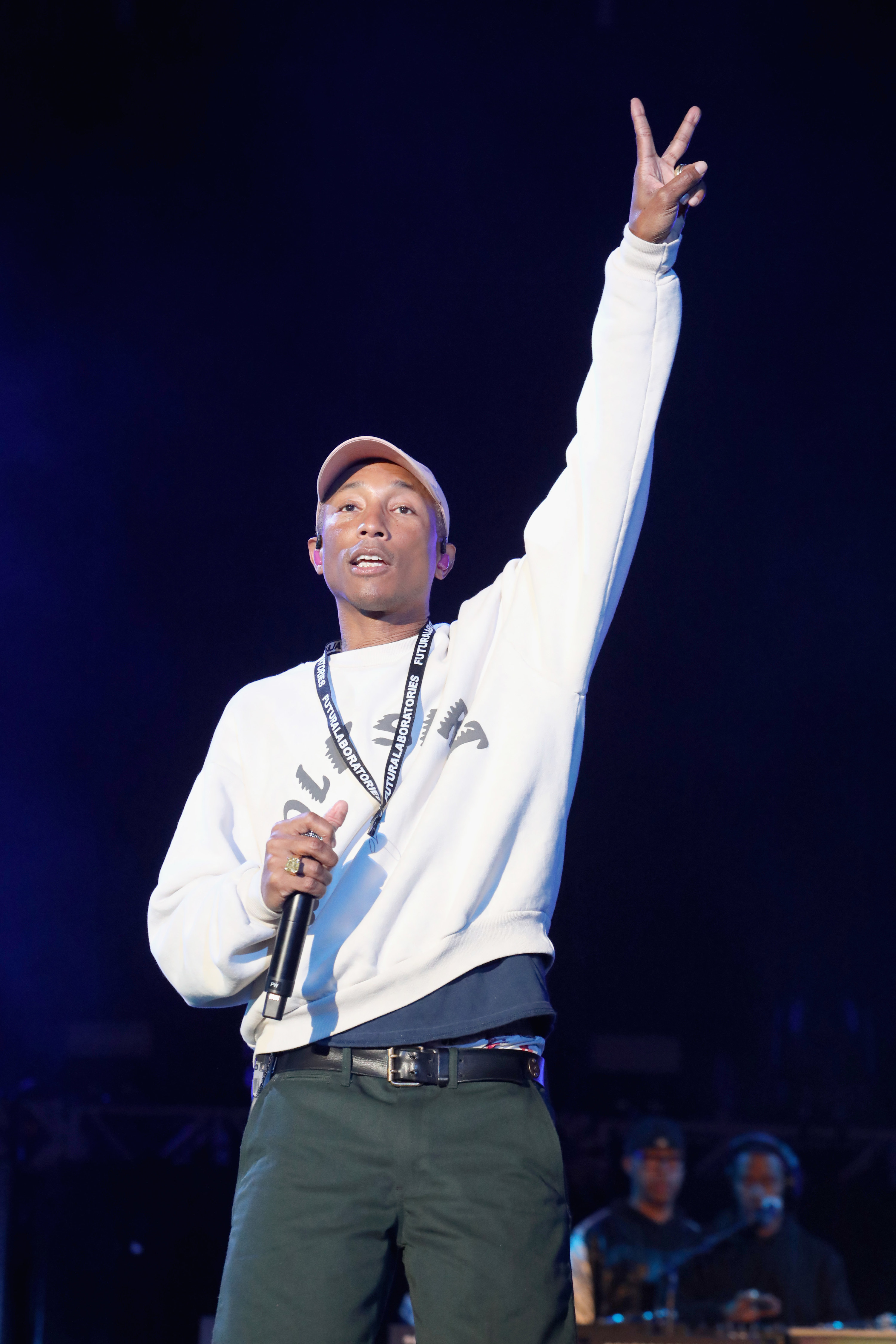 Pharrell standing with one arm raised and holding a microphone in the other