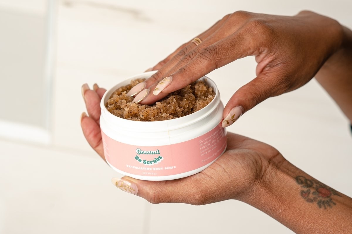 A person holding an open jar of the body scrub