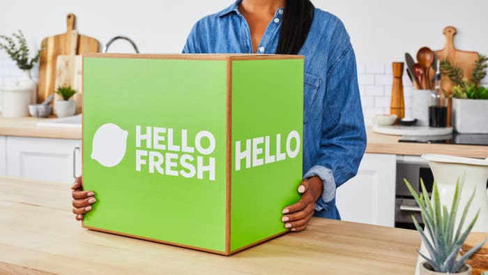 A woman stands in a kitchen with an unopened HelloFresh box.