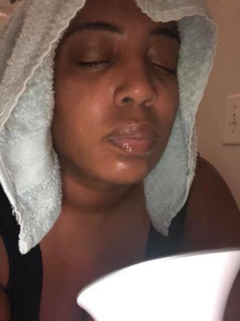 A reviewer uses the facial steamer with a towel over their head
