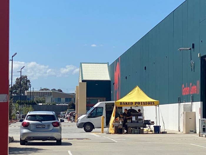 A Bunnings parking lot with a portable yellow pergola stand that is emblazoned with 'BAKED POTATOES'.