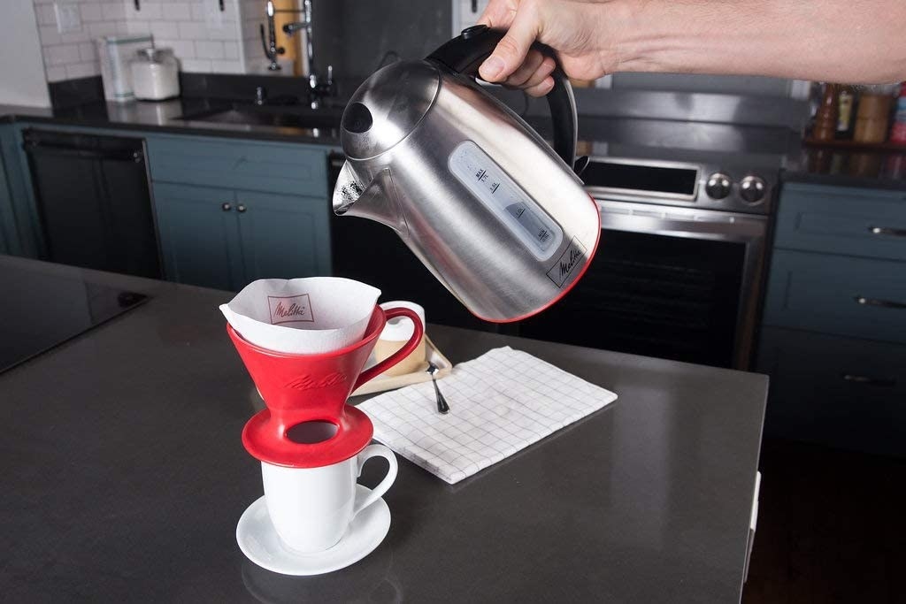 A person pouring water from a kettle over a mug with the coffee dripper placed on top