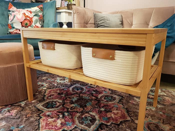 reviewer image of two of the white woven baskets with brown handles on a shelf of a coffee table